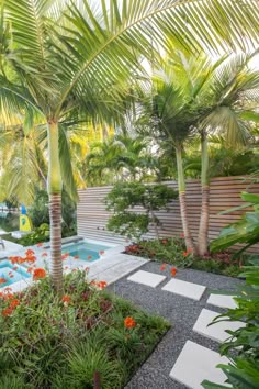 an outdoor swimming pool surrounded by palm trees and flowers in the foreground, next to a stone walkway