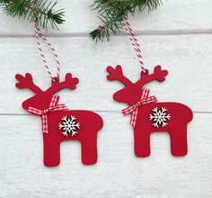 two red wooden reindeer ornaments hanging from a christmas tree on a white wood background with snowflakes