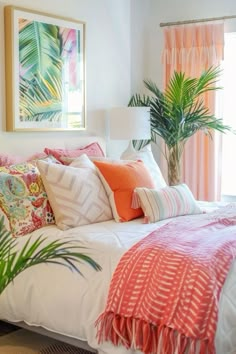 a white bed topped with lots of pillows next to a potted palm tree in front of a window