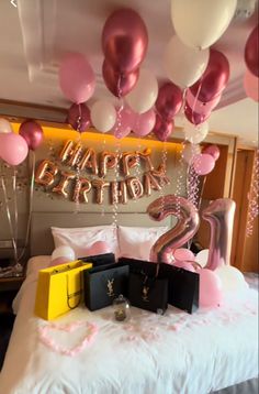 a bed topped with lots of pink and white balloons next to a sign that says happy birthday