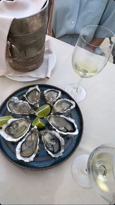 a blue plate topped with oysters next to wine glasses