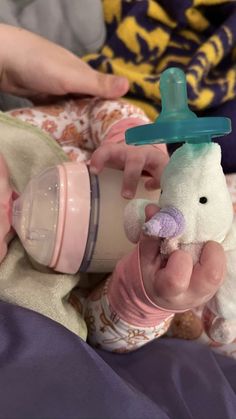 a baby holding a sippy cup with a stuffed animal on it's side