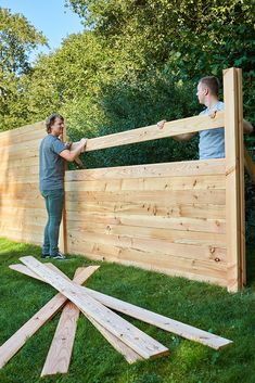 two men are building a wooden fence in the yard with wood planks on the grass