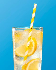 a glass filled with ice and lemons on top of a blue table next to a straw