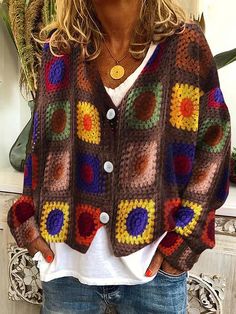 a woman wearing a multicolored crochet cardigan sweater and jeans standing in front of a potted plant