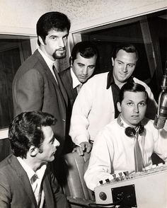 a group of men standing around each other in front of a desk with papers on it