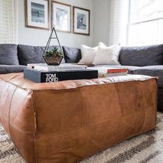 a living room filled with furniture and a book on top of a leather ottoman in front of a window