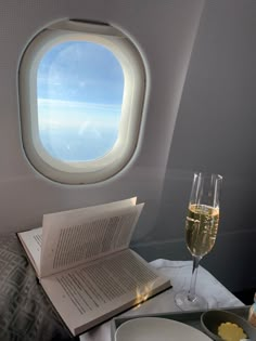 an airplane window with a book and glass of wine