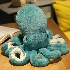 an octopus stuffed animal sitting on top of a wooden table next to a open book