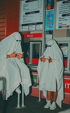 two people in white robes standing next to a vending machine with their faces covered