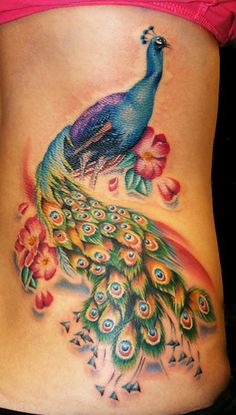 a colorful peacock tattoo on the side of a woman's stomach with flowers and petals