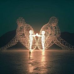 two people standing in the middle of a body of water with lights projected on them