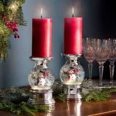 two candles are sitting on a table next to some wine glasses and pine branches with red berries