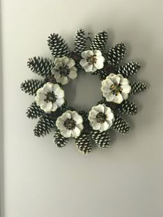 a wreath made out of pine cones and white flowers on the side of a wall