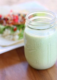 a glass jar filled with green liquid sitting on top of a table next to a plate of food