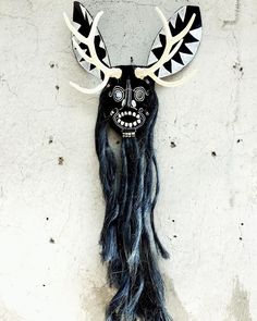 a black and white mask with long hair hanging on a wall next to a brick wall