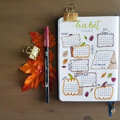 a calendar with autumn leaves and a pen on a wooden table next to an orange maple leaf