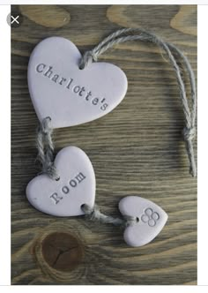 two white ceramic hearts with names on them hanging from twine strings against a wooden background