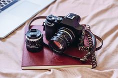 a camera sitting on top of a red book next to a laptop and a pen