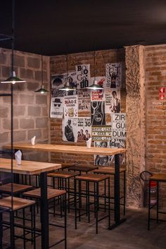 an empty restaurant with wooden tables and stools in front of a brick wall that has posters on it