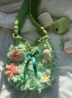 a crocheted purse sitting on top of a bed next to two balls of yarn