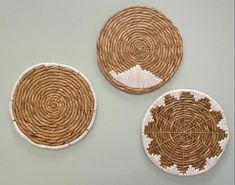 three woven baskets with white and brown designs hanging on the wall next to each other