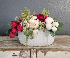 a white vase filled with lots of flowers on top of a wooden table next to a gray wall