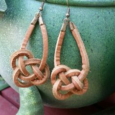 a pair of brown leather earrings on top of a green planter with a pot in the background