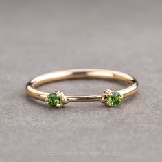 a gold ring with two green stones on the top and bottom, sitting on a gray surface