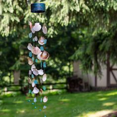 a wind chime with shells hanging from it's side in front of some trees