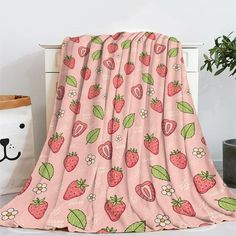 a pink blanket with strawberries on it next to a teddy bear and potted plant