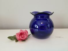 a blue vase sitting next to a pink rose on a white counter top with a wall in the background