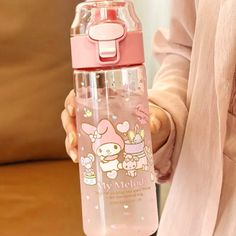 a woman holding a pink water bottle with hello kitty on the side and other items around her