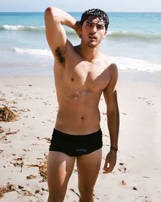 a shirtless man standing on top of a sandy beach next to the ocean with his head in his hands