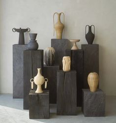 several vases and sculptures are on display in a room with concrete blocks against the wall