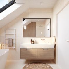 a bathroom with a sink, mirror and bathtub under a slanted skylight