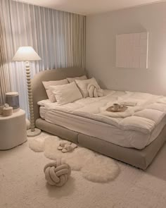 a white bed sitting in the middle of a bedroom next to a lamp and window