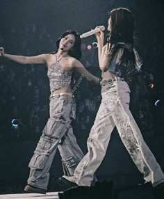 two women on stage with microphones in their hands and one holding her arm out