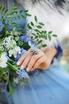 a woman in a blue dress holding a bouquet of white and blue flowers with her hand