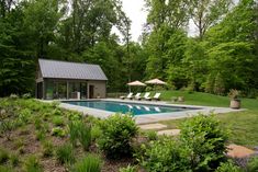 a pool surrounded by lush green trees and bushes with lounge chairs next to the pool