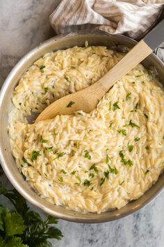 a pot filled with pasta and parsley on top of a marble counter next to a wooden spoon