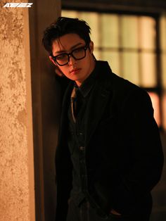 a young man wearing glasses leaning against a wall