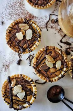 three desserts with chocolate and nuts on top are sitting next to a glass of wine