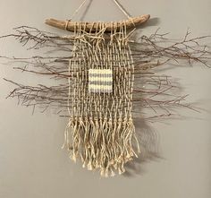 a wall hanging made out of branches and woven material with a small white square in the middle