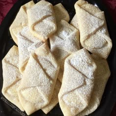 several pieces of powdered sugar on a black plate with a red cloth in the background