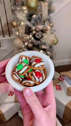 a person holding a small bowl filled with christmas cookies in front of a christmas tree