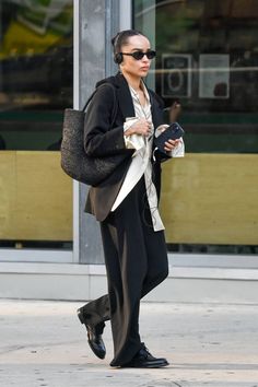 a woman walking down the street in black pants and a blazer with headphones on