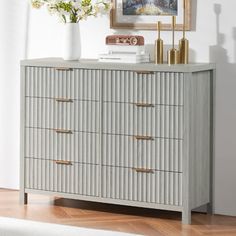 a white vase with flowers on top of it next to a gray chest of drawers