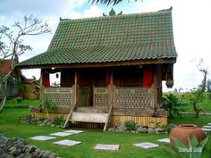 a small wooden house sitting in the middle of a lush green field with stepping stones