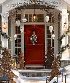 a red front door surrounded by snow covered trees and christmas wreaths with lights on them